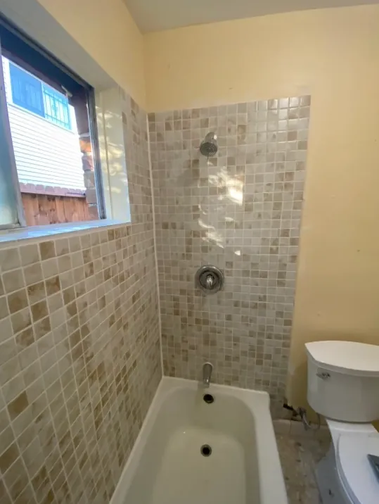 Compact bathroom with warm beige small-square wall tile beside a toilet and tub